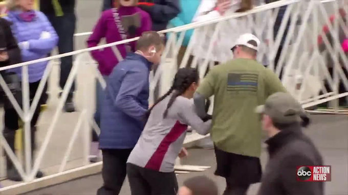 Dua pelari membantu seorang wanita yang berjalan pincang. 